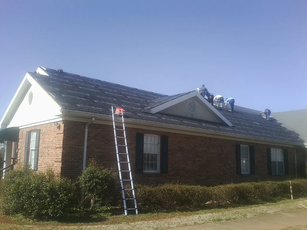 Crew tearing shingles off a brick ranch roof with a ladder set — Metal Roof Repair work by our crew in Ho Ho Kus