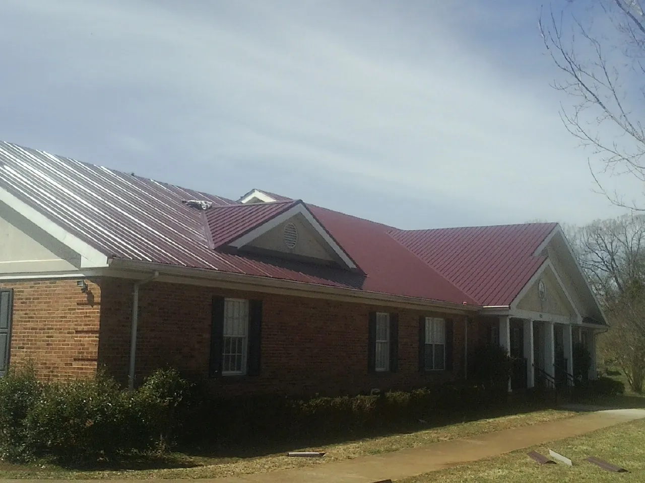 Red metal roof with gabled entries on a long brick building, from a Hail Damage Roof Repair job in Ho Ho Kus