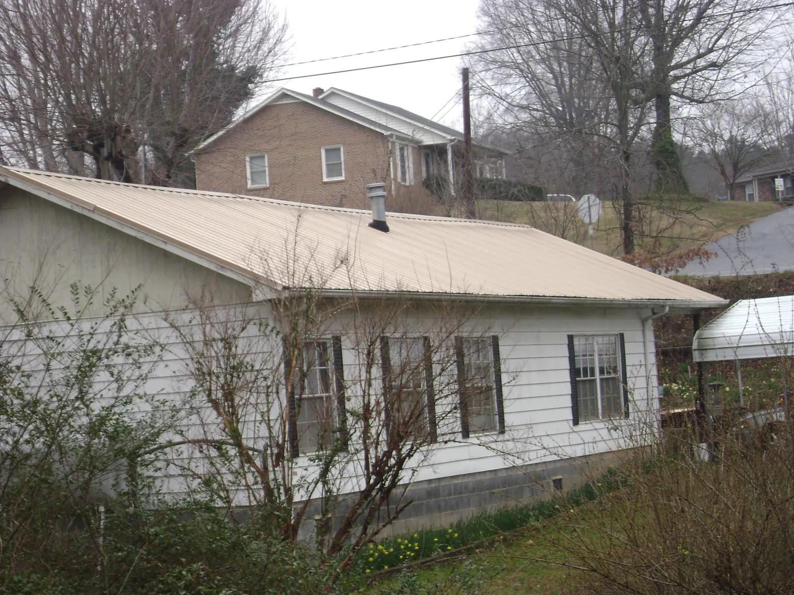 Tan metal roof on a white sided house set into a hillside — Commercial Roofing by Roofing Brothers in Ho Ho Kus